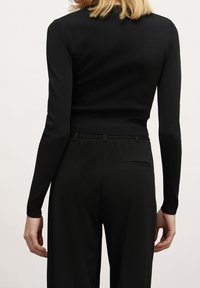 Svart åtsittande tröja med långa ärmar, ribbade muddarn och midja, i kombination med svarta högmidjade byxor som har en slät, mjuk textur.
