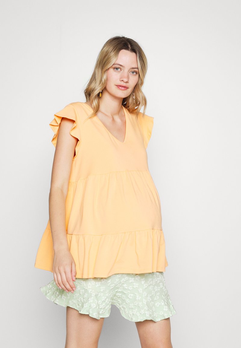 Top peplum em algodão laranja claro com mangas em babados e decote em V, sobre uma saia estampada em flores verde claro com barra em babados.