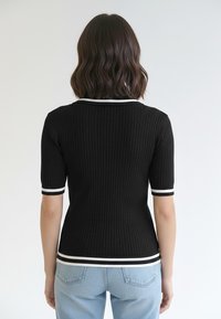 Czarny prążkowany dzianinowy top z krótkimi rękawami, z białymi paskami przy kołnierzu i mankietach rękawów. Widok od tyłu.