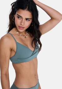 Haut de bikini vert clair à design enveloppant, fines bretelles, et texture lisse. Le collier est orné de petites pièces décoratives.