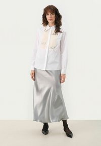White button-up shirt with beige and silver sequined accents, paired with a shiny silver midi skirt. Black pointed flats and tights.