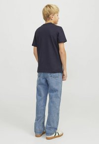 Camiseta de manga corta en navy con cuello redondo, combinada con jeans sueltos de color azul claro y zapatillas blancas con acentos verdes.