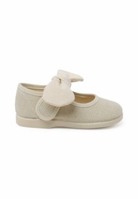 Zapatilla de lona beige con un acabado texturizado, puntera redonda y un lazo decorativo en la correa. Suela plana para mayor comodidad y facilidad de uso.