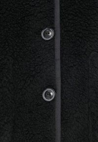 Black fleece coat featuring a textured fabric, a row of black buttons, and a matching ribbon along the closure.