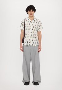 Camisa de manga corta con un estampado de cactus sobre un fondo claro, combinada con pantalones grises de pierna ancha y zapatos negros, luciendo un pequeño bolso bandolera.