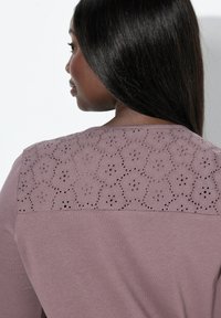 Maglietta a maniche lunghe in tessuto mauve tenue, con uno yoke posteriore in pizzo floreale caratterizzato da dettagli intagliati e una texture liscia.
