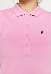 Miękka różowa koszulka polo z mieszanki bawełny, z klasycznym kołnierzykiem, czterema guzikami oraz małym czarnym logo na lewej piersi.