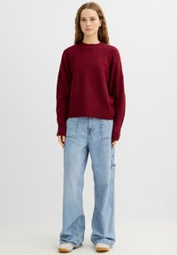 Suéter de punto burdeos con dobladillo acanalado y cuello redondo, combinado con jeans cargo de pierna ancha azul claro con bolsillos laterales y un corte holgado.