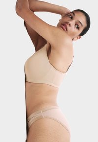 Reggiseno seamless beige chiaro con scollatura moderata e spalline regolabili; mutandine a vita bassa abbinate visibili; texture liscia.