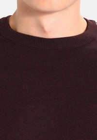 Maroon knit sweater featuring a round neckline and a soft texture. The fabric shows a subtle pattern with slight variations in color.