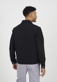 Giacca nera con design a colletto, maniche lunghe e dettagli in bottone argentato. Il tessuto appare liscio con una silhouette moderna.