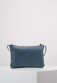 Borsa a tracolla in pelle blu con forma rettangolare, chiusura con zip nella parte superiore e una singola tracolla. Texture liscia con accenti minimi.