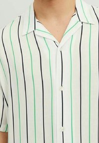 Biała koszula z kołnierzykiem w pionowe czarne i zielone paski, zapięta na guziki, pokazana od szyi do połowy torsu.
