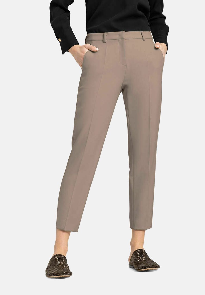 Beige maatwerkbroeken met een slim fit, voorzien van zijzakken en een zachte textuur. G gedragen met een zwarte top en metalen loafers.