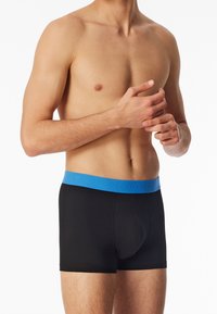 Boxer slip neri con un elastico azzurro che presenta il nome del brand. Tessuto morbido, vestibilità aderente, design di lunghezza media.