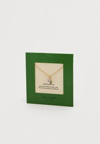 Zelta ķēdes kaklarota ar mazu ziedu piekariņu ar violetu ziedu un zaļām lapām, izvietota zaļā kartītē ar pateicības tekstu.