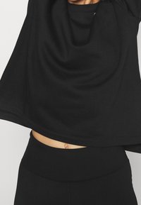 Sweatshirt noir cropped avec une coupe décontractée et une texture douce, associé à des leggings noirs taille haute. Peau visible au niveau du ventre.