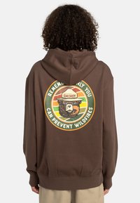 Sweat à capuche marron avec un graphique circulaire au dos, représentant un ours portant un chapeau, avec un slogan sur la prévention des incendies de forêt.