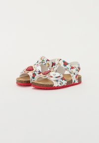 White sandals with floral print, red accents, and heart-shaped embellishments. Cork sole and adjustable straps. Flat design for comfort.
