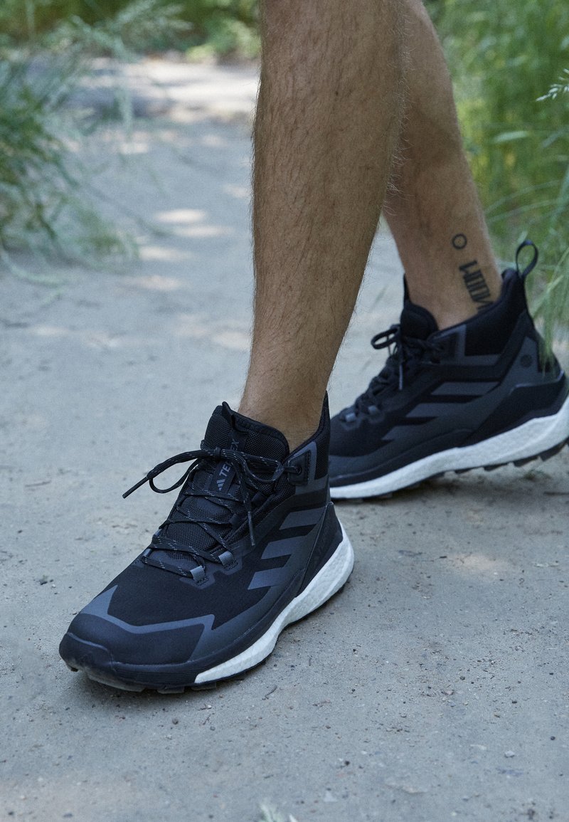 Zwarte sportieve schoenen met een synthetisch bovenwerk, gestructureerde veters en een contrasterende witte zool. Bevat drie diagonale strepen en een versterkte hiel.