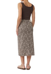 Brązowy top na ramiączkach w połączeniu z spódnicą o średniej długości, zdobioną wzorem w panterkę w odcieniach brązu i beżu, uzupełnioną płaskimi sandałami.