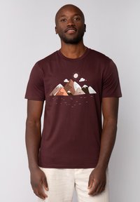 Weinrote T-Shirt mit einem Bergmotiv in Brauntönen, Weiß und Grün, darunter Sonne und Wolken. Kurze Ärmel und runder Halsausschnitt.