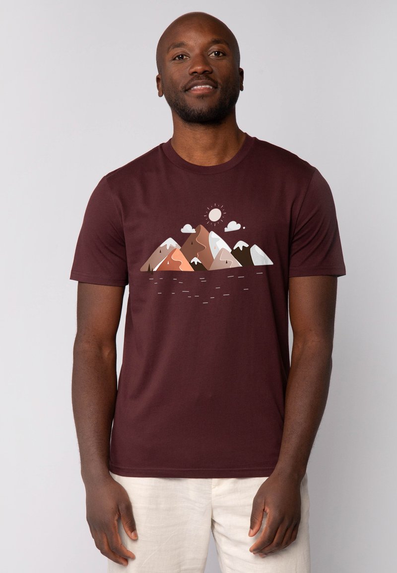 Weinrote T-Shirt mit einem Bergmotiv in Brauntönen, Weiß und Grün, darunter Sonne und Wolken. Kurze Ärmel und runder Halsausschnitt.