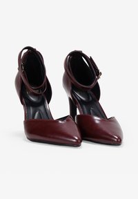 Zapatos de tacón alto de cuero burdeos con puntas afiladas y tiras en los tobillos, con un acabado suave y una silueta delgada y elegante.