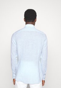 Ljusblå randig långärmad skjorta med skräddarsydd passform, knappmanschetter och standardkrage. Tyget verkar slätt och lätt.