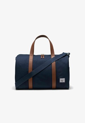 Sac de sport en toile bleu marine avec des poignées et des accents en cuir marron, fermeture éclair et bandoulière réglable. Comprend un petit patch logo à l'avant.