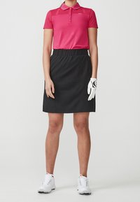 Rosa pikétröja med korta ärmar och randig struktur, ihop parat med en svart kjol med elastisk midja, vita golfskor och en vit handske.