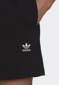 Mustat urheilushortsit, joissa on tekstuuroitu puuvillakangas ja valkoinen brodeerattu Adidas-logo helmassa.
