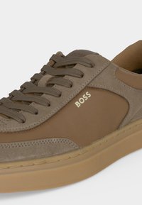 Baskets en daim et tissu marron avec lacets assortis, semelle beige et logo "BOSS" sur le panneau latéral.