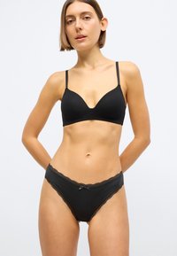 Zwarte lingerie set met een naadloze, diep uitgesneden beha en bijpassende slip met kanten rand en een kleine strik op de tailleband.