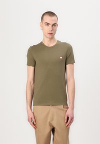 Oliven grøn kortærmet T-shirt lavet af glat stof, med et lille rødt trekantet logo på venstre bryst. Sidder tæt til kroppen.