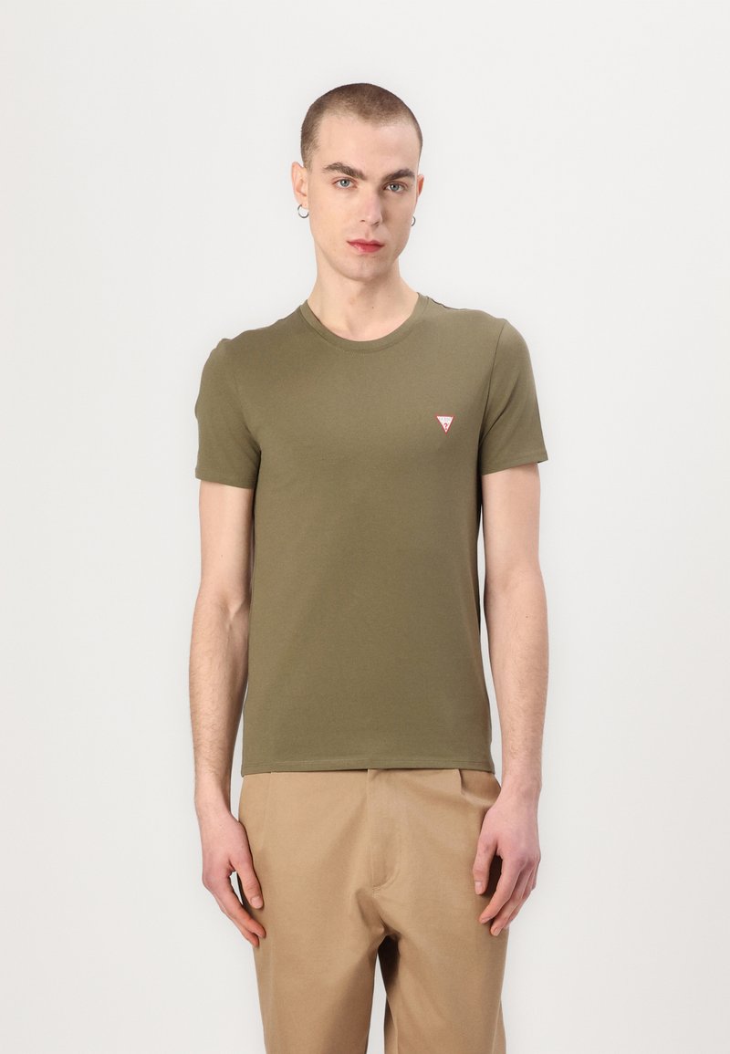 Oliven grøn kortærmet T-shirt lavet af glat stof, med et lille rødt trekantet logo på venstre bryst. Sidder tæt til kroppen.