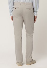 Pantaloni grigi chiari realizzati in tessuto liscio, con tasche posteriori dotate di bottoni. Abbinati a espadrillas beige e a una camicia a righe.