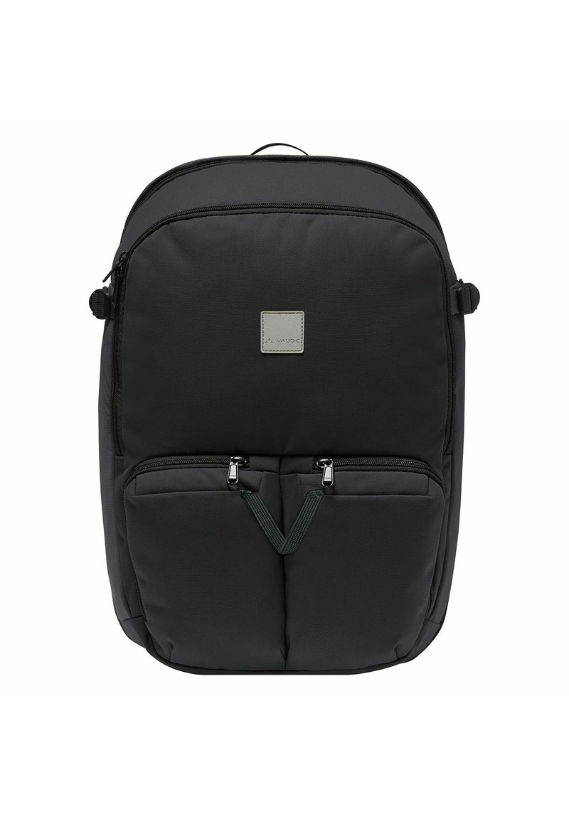 Zaino in nylon nero con forma arrotondata, dotato di due tasche anteriori con zip, una patch con logo e spallacci regolabili. Texture liscia, design minimalista.