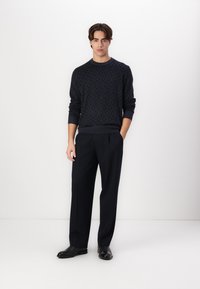Donkerblauwe trui met diamantpatroon, ronde hals, geribde manchetten, gecombineerd met nauwsluitende donkere broek en stijlvolle zwarte schoenen. Eenvoudig, modern ontwerp.