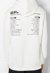 Sudadera blanca con la lista de canciones del álbum impresa en negro en la parte posterior. El diseño incluye una capucha con cordón y puños y dobladillo acanalados.