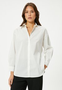 Camicia bianca con colletto classico, maniche lunghe e vestibilità comoda. Realizzata in tessuto liscio con una leggera lucentezza e senza motivi.