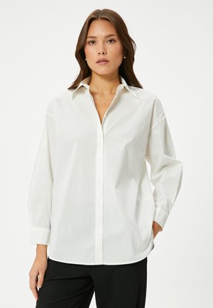Camicia bianca con colletto classico, maniche lunghe e vestibilità comoda. Realizzata in tessuto liscio con una leggera lucentezza e senza motivi.