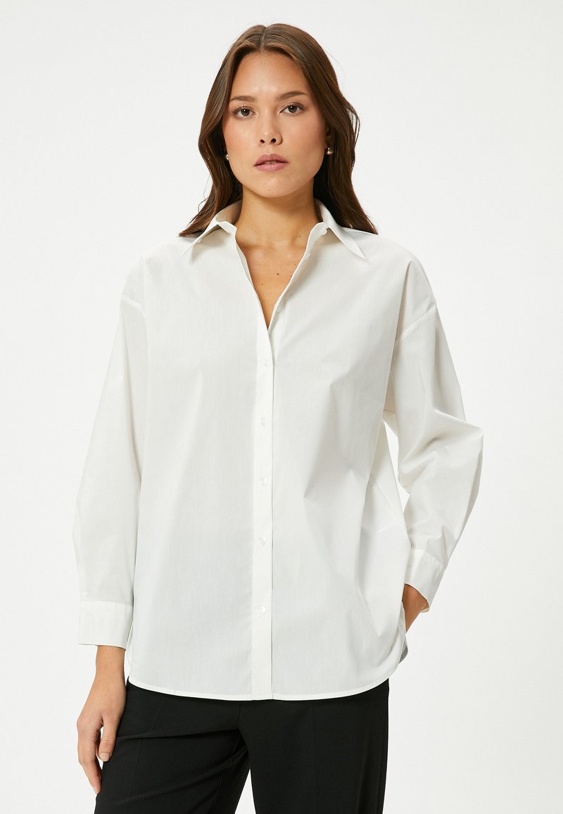 Camicia bianca con colletto classico, maniche lunghe e vestibilità comoda. Realizzata in tessuto liscio con una leggera lucentezza e senza motivi.