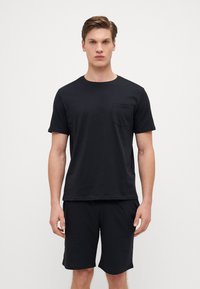 Schwarzes Baumwoll-T-Shirt mit kurzen Ärmeln und einer Brusttasche, kombiniert mit passenden schwarzen Shorts, die beide ein schlichtes, glattes Design aufweisen.