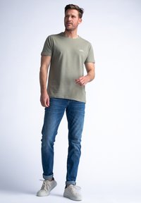 Camiseta de algodón verde oliva de manga corta y cuello redondo acanalado, combinada con jeans de denim azul y zapatillas ligeras.