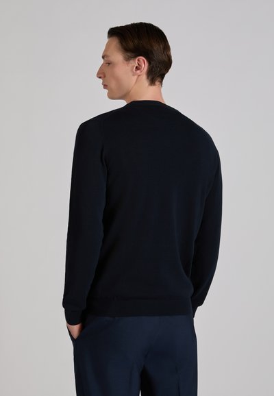 Navy blue pullover sweater, ribbed neckline and cuffs, smooth texture, with long sleeves, worn over matching dark trousers.