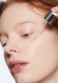 Heldropperfles die een serum op een gladde, doorzichtige huid dispenseert; lichtroze lippen; lichte huidtint; minimalistische achtergrond.