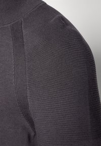 Grauer Strickoberteil mit hohem Kragen, gerippten Schulternähten und strukturiertem Stoffdesign, das eine glatte, enganliegende Passform betont.