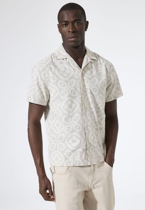 Korte mouw overhemd met knopen in lichtbeige met een geometrisch patroon en een gestructureerde stof. Gecombineerd met lichtgekleurde broek.