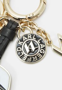 Nyckelring med en guldfärgad metallring, svart läderrem och en rund medaljong med "KARL LAGERFELD" präglat i vit text.